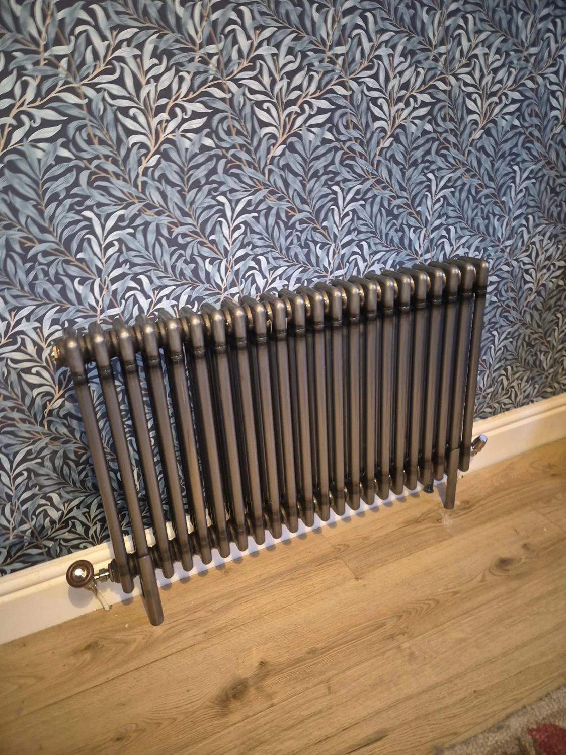 Decorative dark column radiator installed against patterned wallpaper