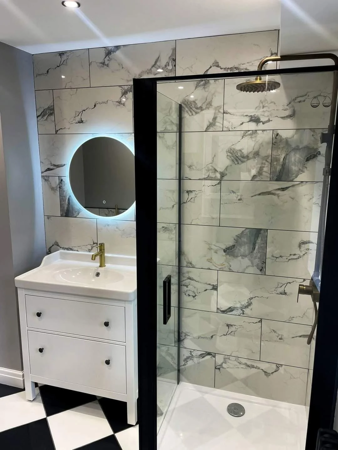 Marble-effect shower enclosure with brass fittings and an illuminated round mirror