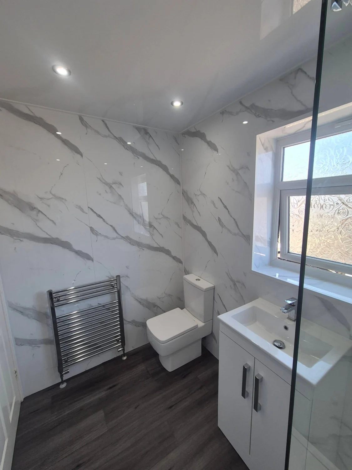 Completed marble-effect bathroom with shower screen, vanity, toilet and chrome towel radiator